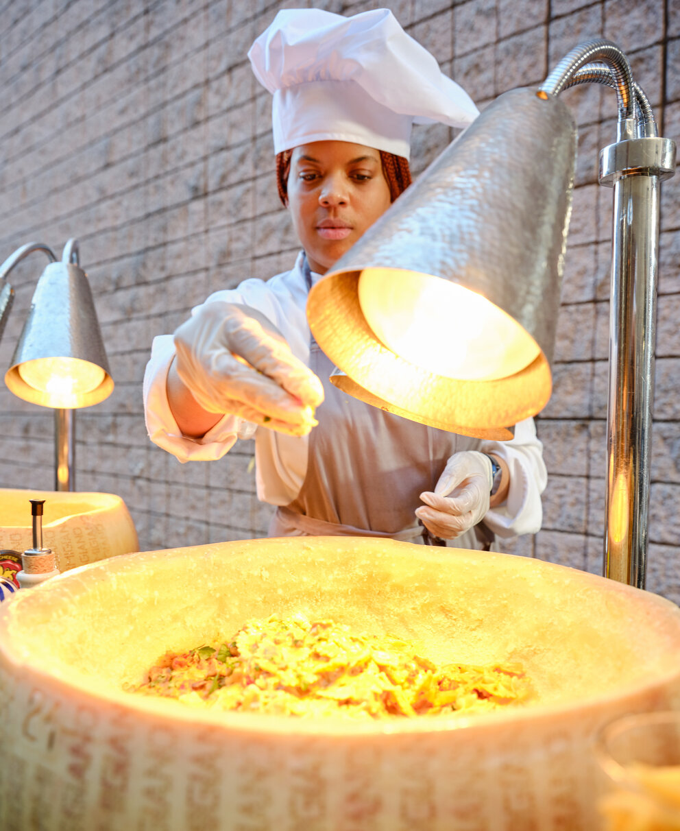A chef garnishing pasta in a parmesan wheel