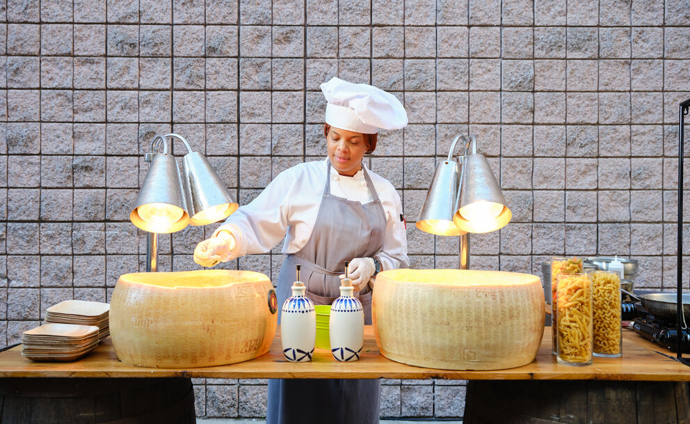 a woman in chefs hat standing at a table with cheeses